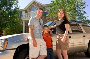 Una familia sonriente junto a su SUV plateada frente a su casa